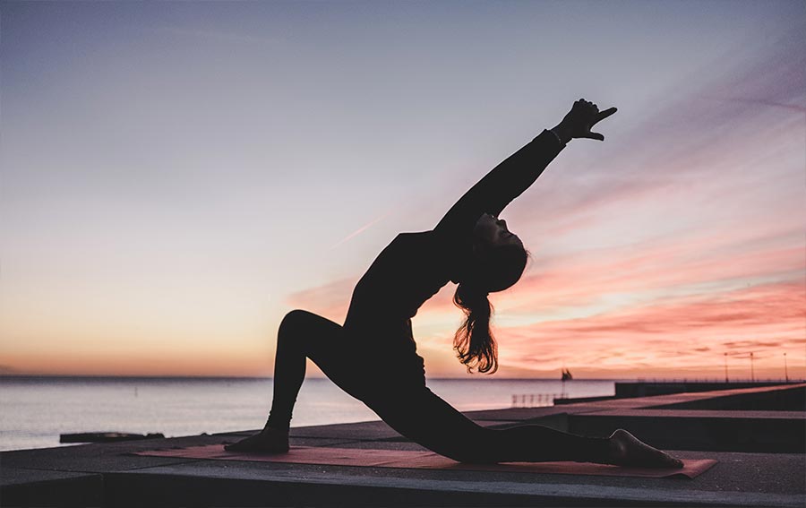 A female doing yoga at sunset. Photo by Kike Vega at Unsplash.