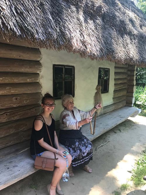 In an open-air museum, an old woman is showing weaving skills to a young female visitor.