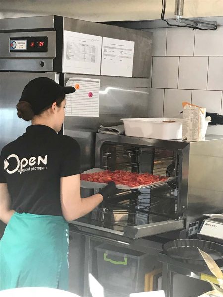 A fast food restaurant employee is putting a food tray in the oven.